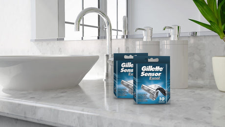 Two packs of Gillette Sensor Excel razor blades on a white marble bathroom worktop beside a chrome tap and basin