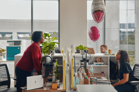 Colleagues chatting in an office with an HP printer and birthday balloons nearby