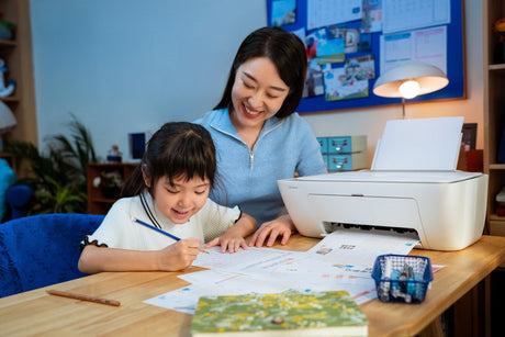 Mother and daughter smiling together at a desk with an HP printer, doing homework