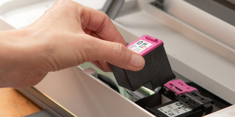 Hand inserting an HP 64 tri-colour ink cartridge into a printer